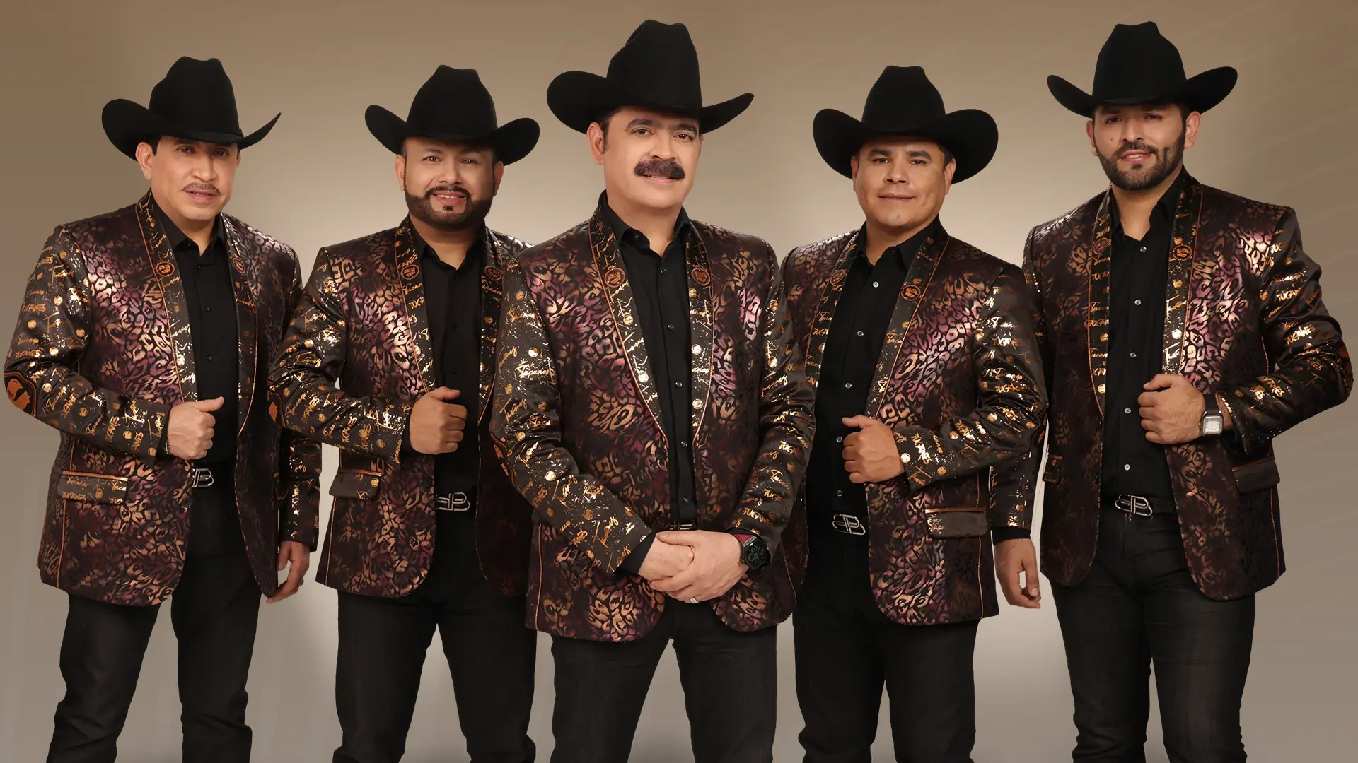 Los Tucanes band members dressed for performance, standing in a line in front of a tan background